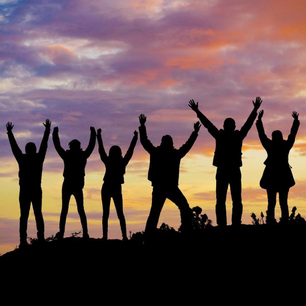 Silhouette of people on a hill, arms raised against a backdrop of a sunset for us with Heroes concert