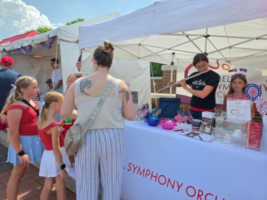 Mom and two kids at CarmelFest booth watching Carmel Symphony musician play the flute.