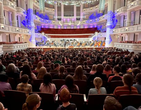 A photo of a student audience from behind them in the Payne & Mencias Palladium with orchestra on stage