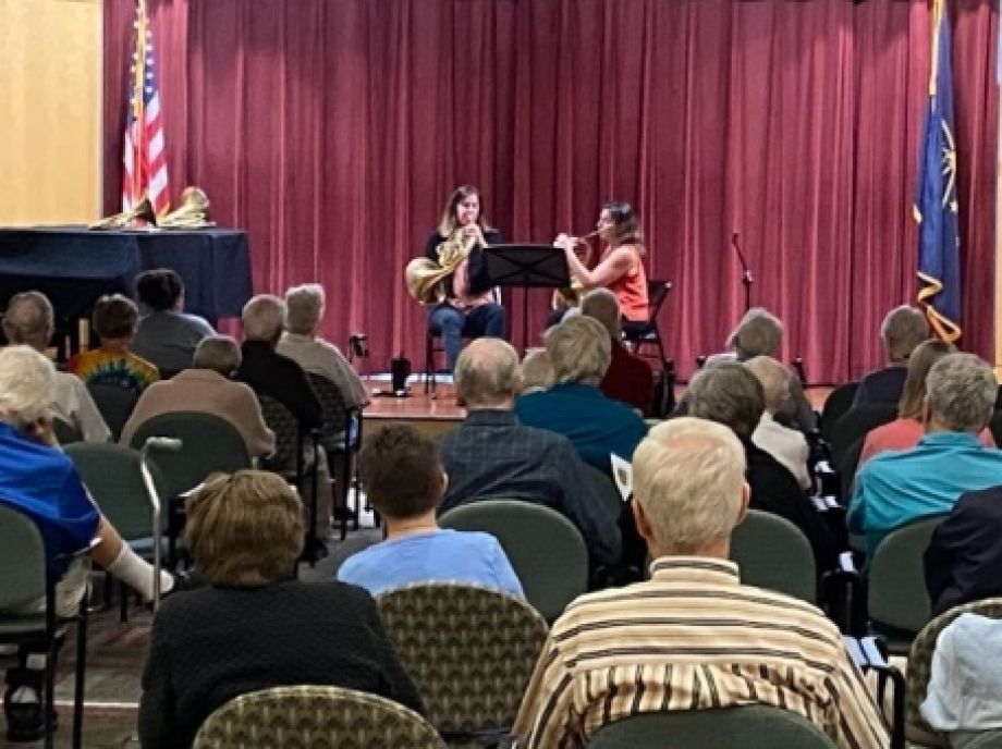Two Carmel Symphony horn players on stage at Marquette Manor Senior Living Center.