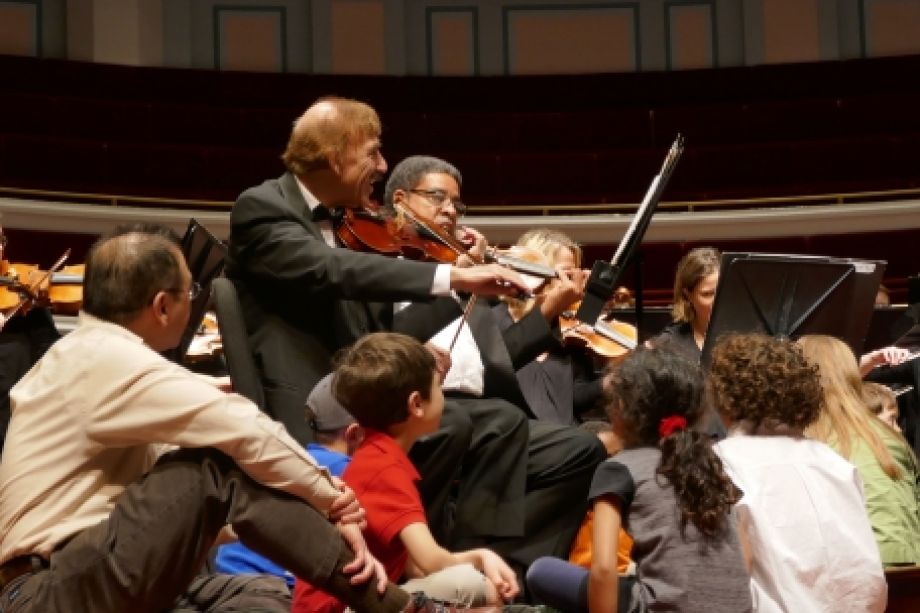 Kids sitting on stage among the instruments and musicians during the Family Fun concert to inspire a love of classical music.