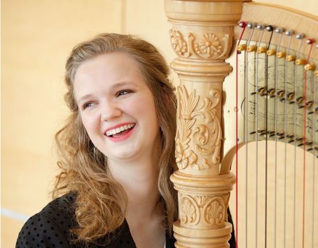 Melanie Mashner - female in black jacket with intricately carved harp leaning against her shoulder.