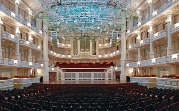 interior of the Payne & Mencias Palldium empty with maroon seats, cream colored wall, and light blue light on the ceiling showing behind the glass acoustical panels mounted from the ceiling.
