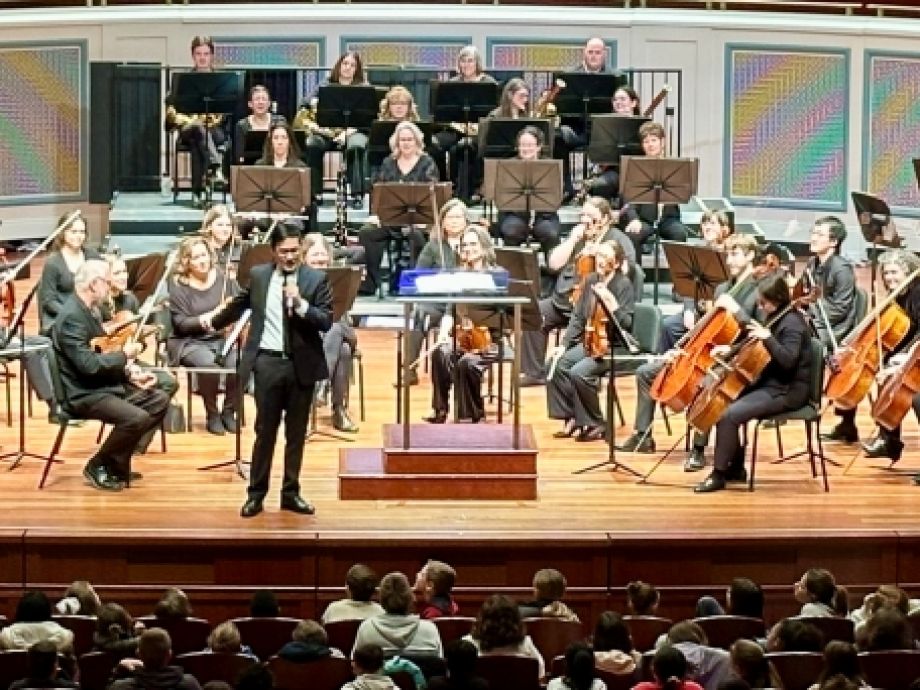 Conductor Thomas Chen stands on stage with the Carmel Symphony Orchestra talking to the students attending Music Matters concert