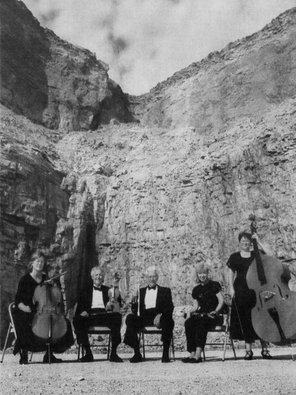 Black and white photo of five musicians and instruments in a rock quarry. This photo was used for the "Concert in the Quarry" event.