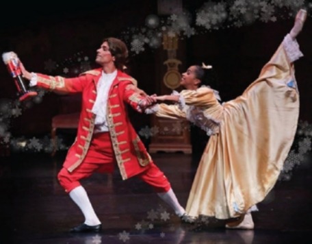 Male danseur in red 1820 formal long jacket holding the Nutcracker toy and female ballerina in 1820s style long gown dancers depicting a scene from the Nutcracker ballet where he is trying keep the Nutcracker toy from her.