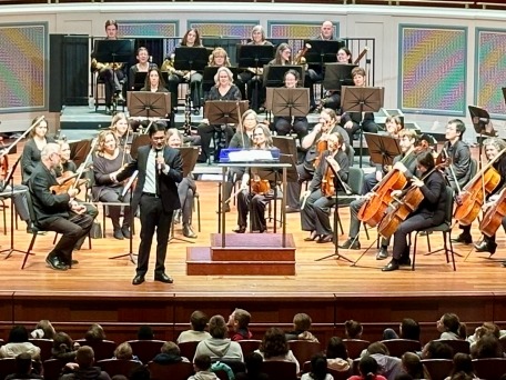 Conductor Thomas Chen stands on stage with the Carmel Symphony Orchestra talking to the students attending Music Matters concert