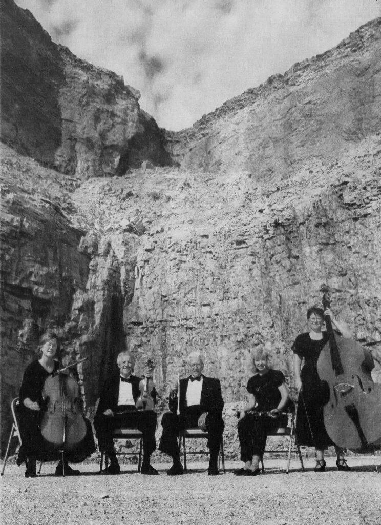 Black and white photo of five musicians and instruments in a rock quarry. This photo was used for the "Concert in the Quarry" event.