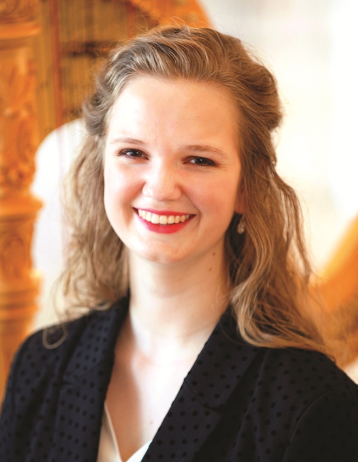 Carmel Symphony Orchestra's Principal Harp player, Melanie Mashner in black blazer seated in front of a ornately carved harp