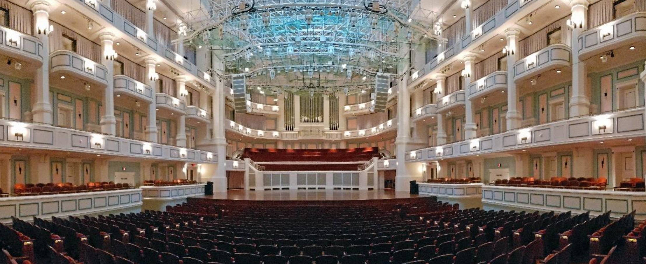 interior of the Payne & Mencias Palldium empty with maroon seats, cream colored wall, and light blue light on the ceiling showing behind the glass acoustical panels mounted from the ceiling.