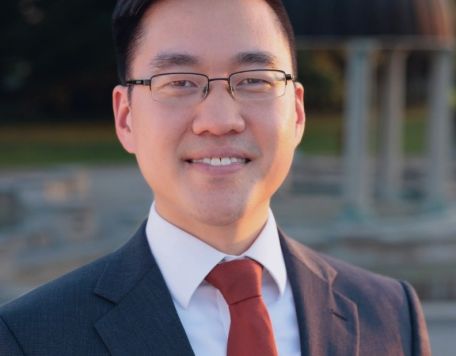 Thomas Chen - in a dark suit, white shirt and red tie. He is Director of Orchestras at Carmel High School and conductor for the educational concert - Music Matters