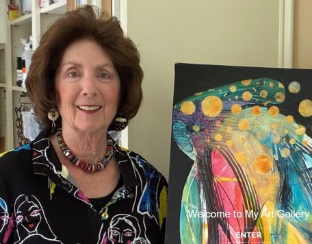 Marianne Glick poses in bright colored blouse with a colorful painting she created.