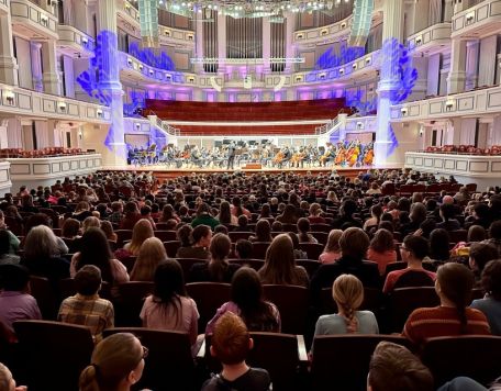 A photo of a student audience from behind them in the Payne & Mencias Palladium with orchestra on stage