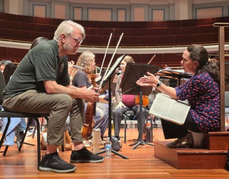 Musicians on stage during practice talking with guest conductor Kelly Corcoran